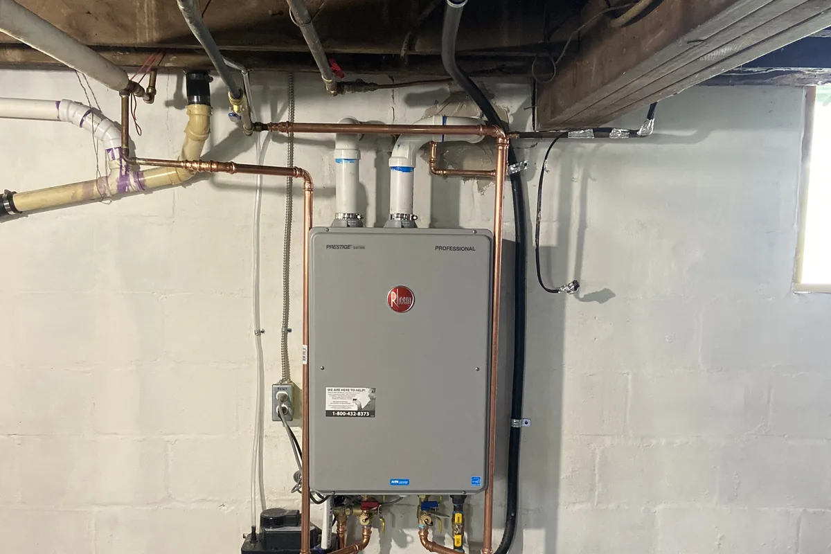 Tankless gas water heater with new copper piping installed on a basement wall by J&K Heating & Cooling